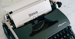 Schwarze Olympia-Schreibmaschine mit einem Blatt Papier, auf dem das Wort "News" steht.
